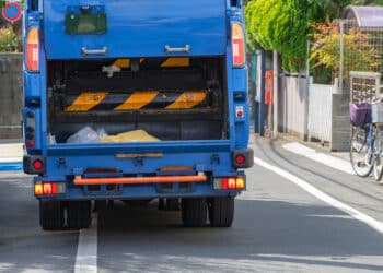 Caminhão de lixo azul realizando coleta urbana em via residencial durante o dia