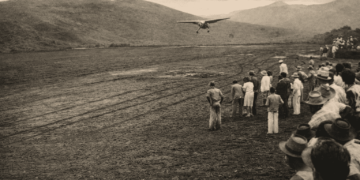 Avião pousando em antigo campo de aviação em Itabira com moradores assistindo ao redor