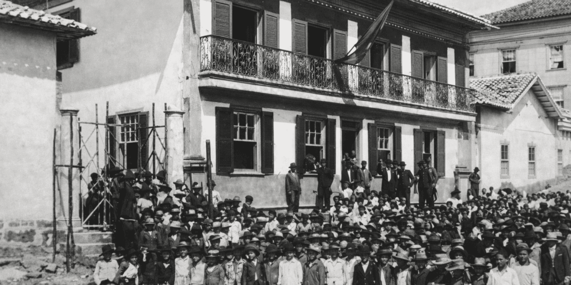 Antiga escola Coronel José Batista em Itabira com grande grupo de alunos reunidos em frente ao prédio histórico no início do século XX