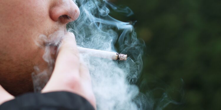 Pessoa fumando cigarro com fumaça ao redor em imagem sobre nova lei do Reino Unido contra tabagismo entre jovens