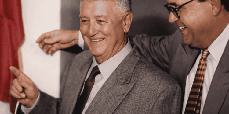 Mauro Ribeiro sorrindo em evento oficial em Itabira ao lado de outro homem de terno