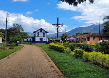 Vista do centro da Serra dos Alves, em Itabira, com capela azul e branca, casas antigas, jardim e montanhas ao fundo