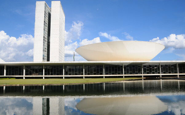 Prédio do Congresso Nacional, em Brasília, com torres e cúpula refletidas no espelho d’água, usado em notícia sobre deputados de Minas e escala 6x1.
