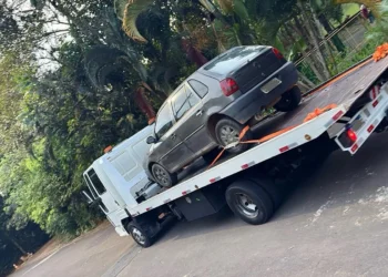 Caminhão-guincho transportando carro em via arborizada, representando serviço de reboque e auto socorro em Itabira.