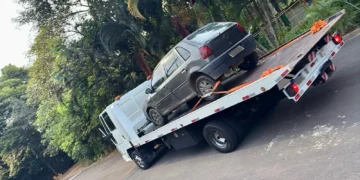 Caminhão-guincho transportando carro em via arborizada, representando serviço de reboque e auto socorro em Itabira.