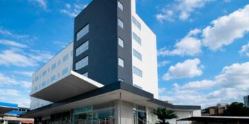 Fachada do Premium Executive Hotel em Itabira, com prédio moderno, céu azul e área de entrada do hotel.