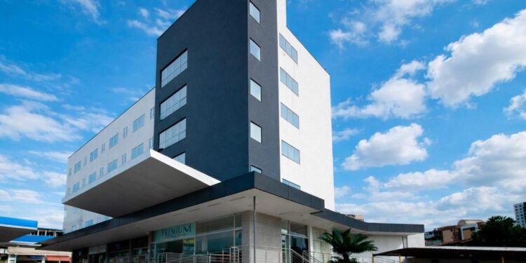 Fachada do Premium Executive Hotel em Itabira, com prédio moderno, céu azul e área de entrada do hotel.