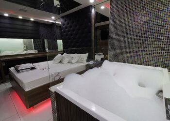 Suíte de motel em Itabira com cama, espelhos, iluminação moderna e banheira de hidromassagem com espuma.