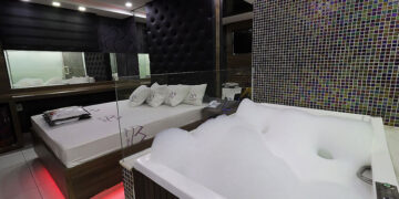 Suíte de motel em Itabira com cama, espelhos, iluminação moderna e banheira de hidromassagem com espuma.